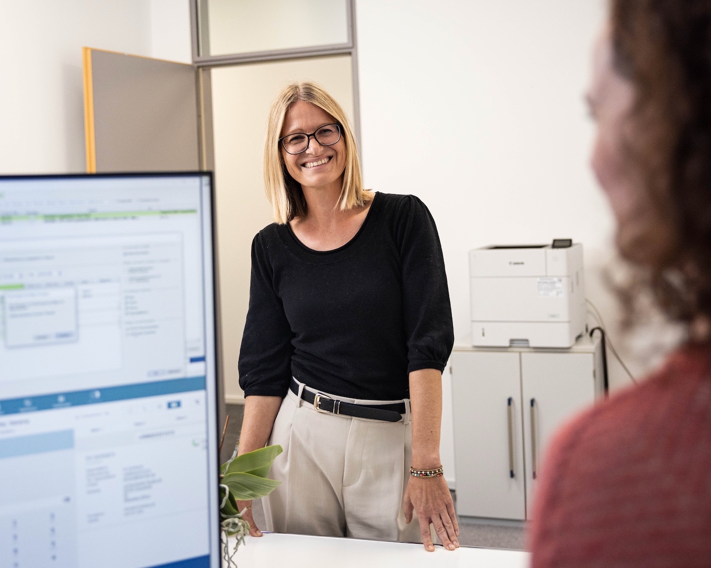 Mitarbeiterin steht an einem Schreibtisch einer Kollegin